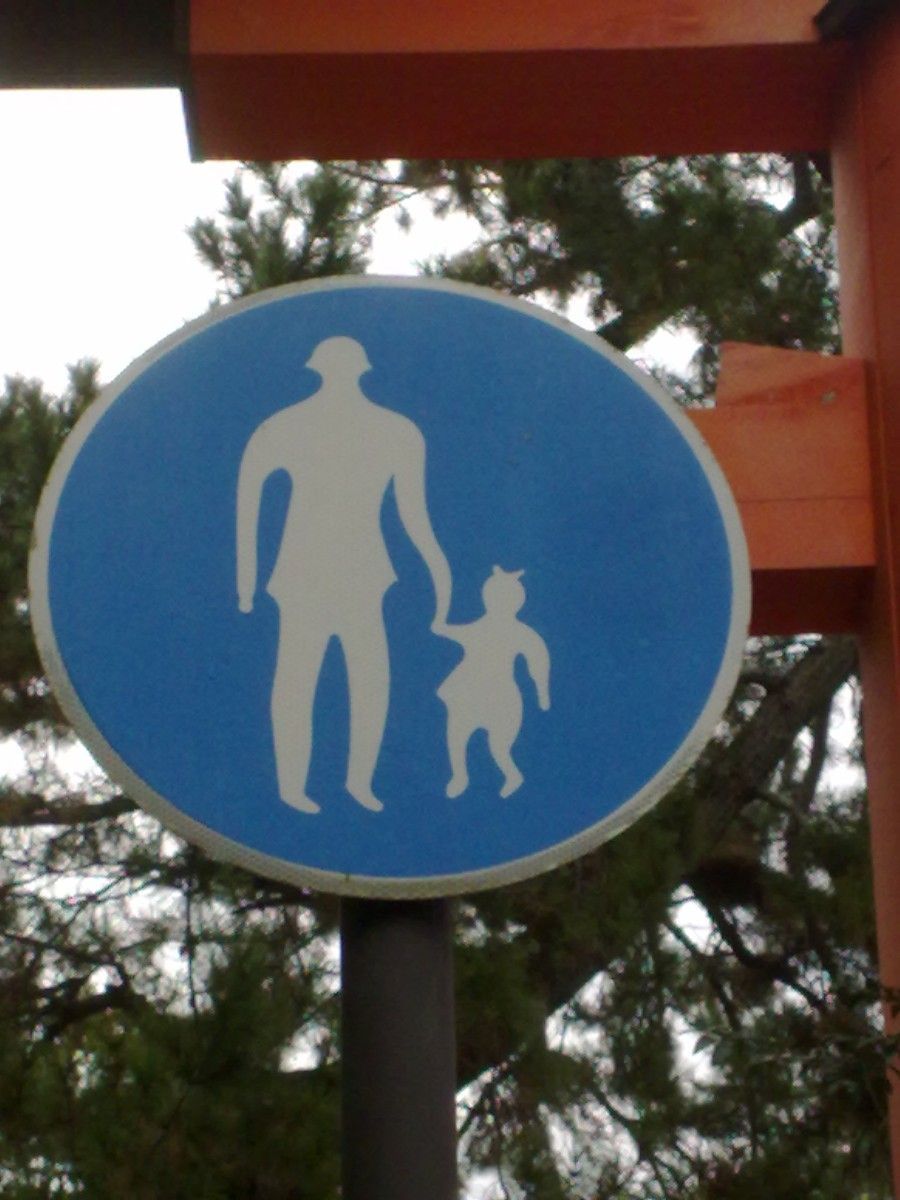 A white on blue traffic sign showing soft forms of an adult and a child, all in curvy design

Part of a red torii is visible, as well as branches