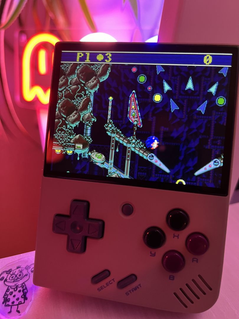 Sonic Spinball playing on a handheld gaming device in front of a neon light.