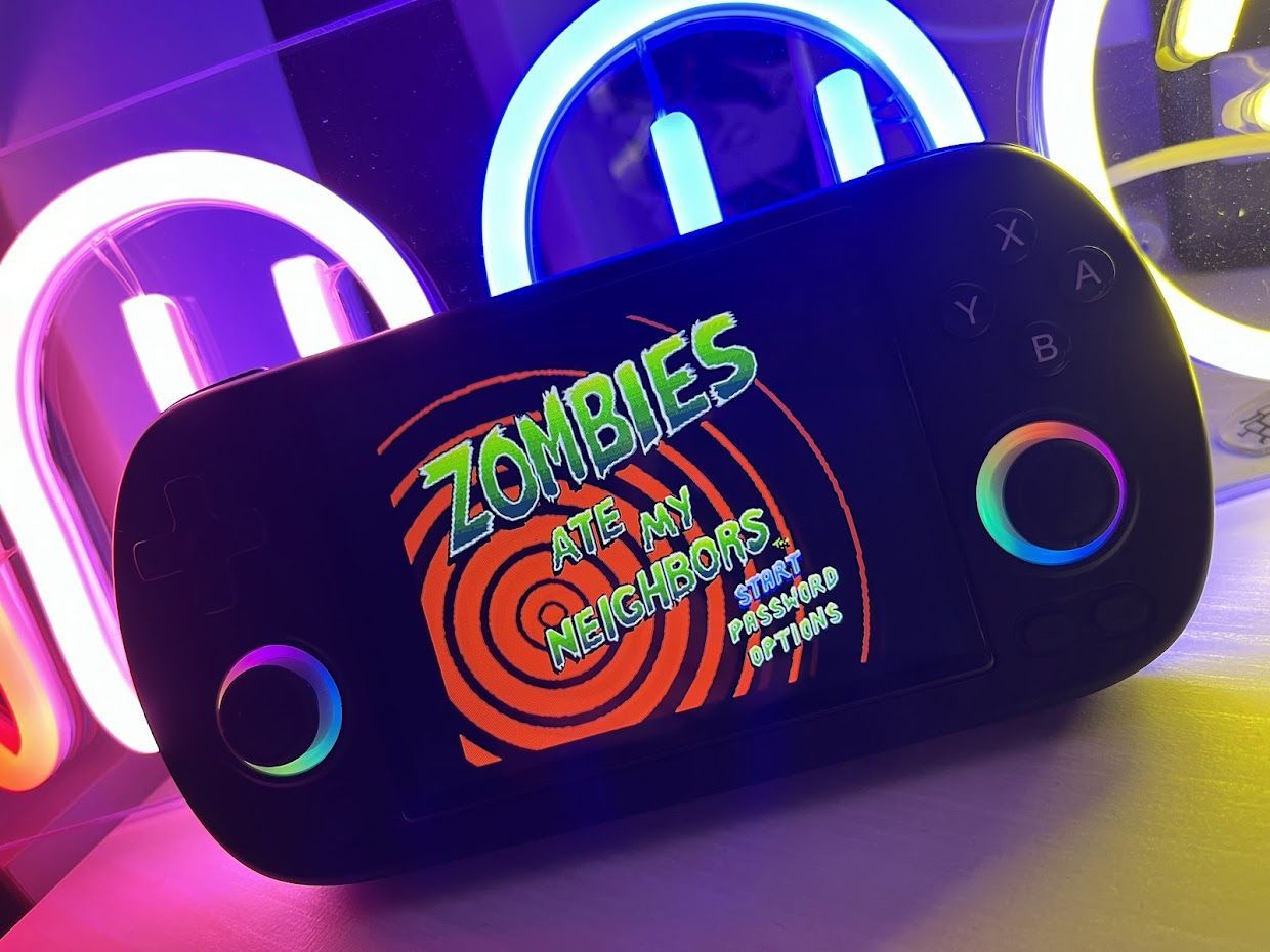 A handheld gaming console displays the title screen of the game "Zombies Ate My Neighbors." The background has colorful neon lights in purple, blue, and yellow, enhancing the vibrant aesthetic.