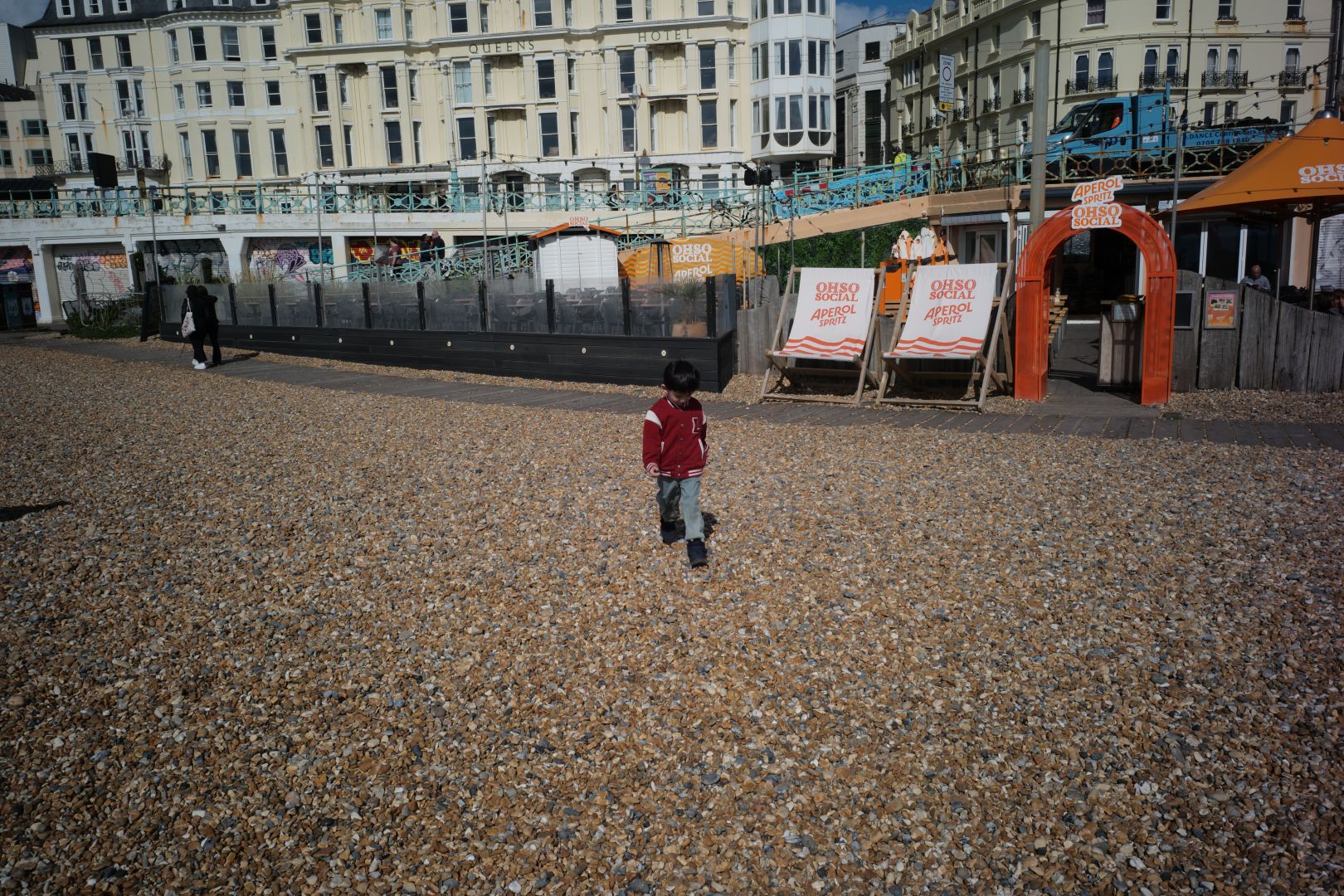 A boy in a red jacket standing on a pebble beach